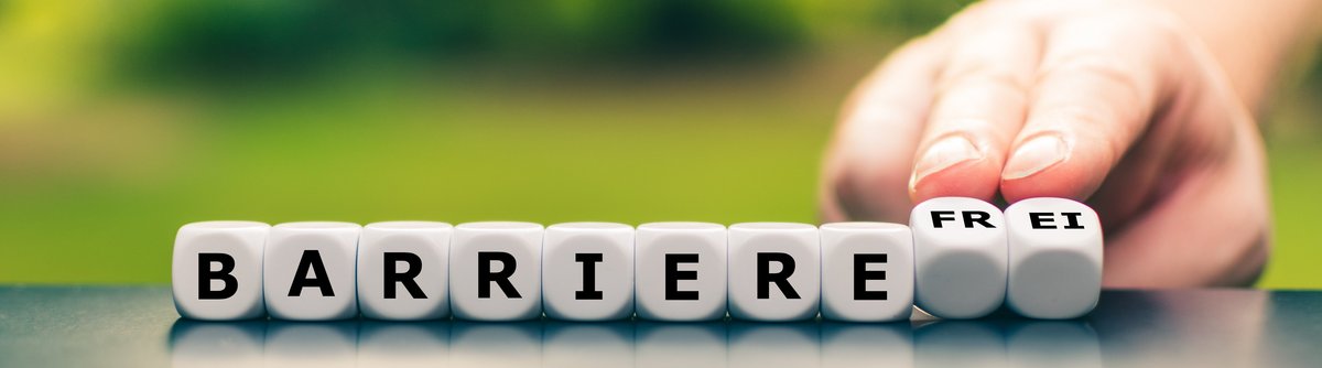 Würfel mit Buchstaben, die das Wort Barrierefrei buchstabieren. Eine Hand dreht die letzten vier Würfel von blanko zu frei.